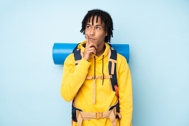 Young mountaineer african american man with a big backpack isolated on a blue wall thinking an idea