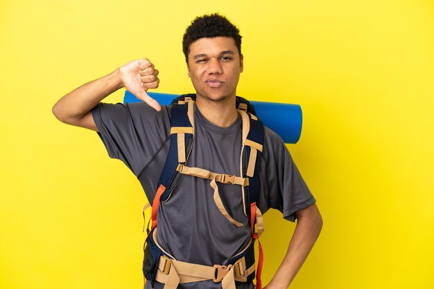 Photo young mountaineer african american man with a big backpack isolated on yellow background showing thumb down with negative expression