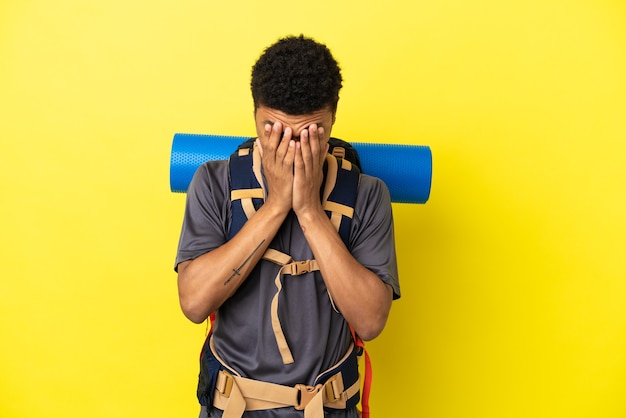 疲れたと病気の表情で黄色の背景に分離された大きなバックパックを持つ若い登山家アフリカ系アメリカ人の男