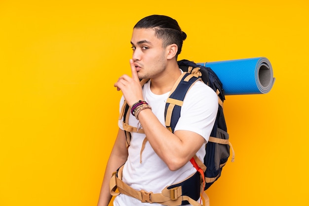 Young mountaineer asian man with a big backpack isolated on yellow background doing silence gesture