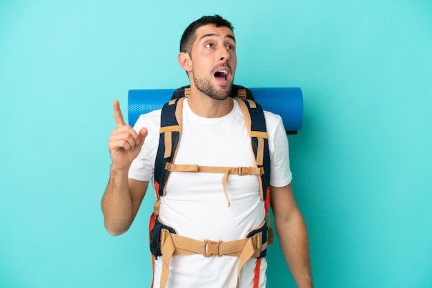 Young mountaineer caucasian man with a big backpack isolated on blue background intending to realizes the solution while lifting a finger up