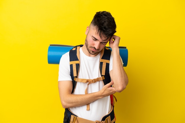 Young mountaineer caucasian man with a big backpack isolated on yellow background with headache