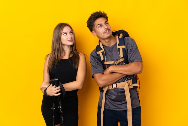 Young mountaineer couple with a big backpack on yellow looking up while smiling