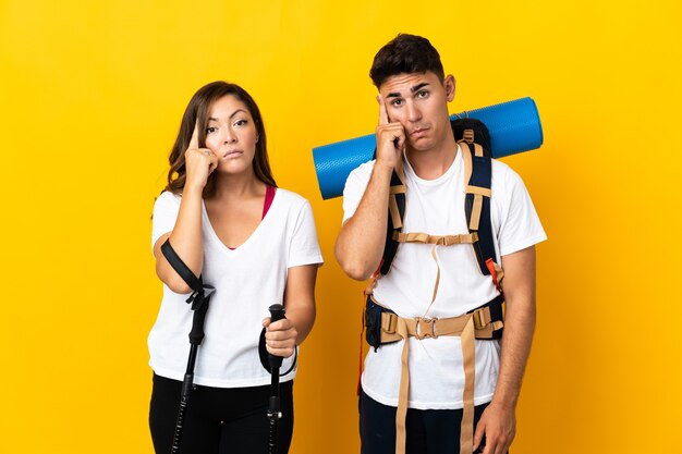 Young mountaineer couple with a big backpack on yellow thinking an idea