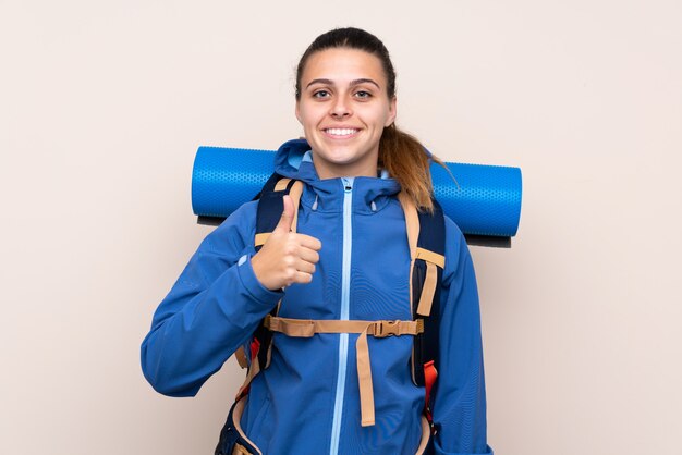 Молодая девушка альпинист с большим рюкзаком, давая пальцы вверх жест
