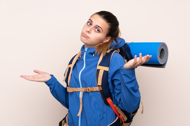 Young mountaineer girl with a big backpack having doubts with confuse face expression