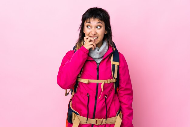 Young mountaineer girl with a big backpack over isolated pink nervous and scared