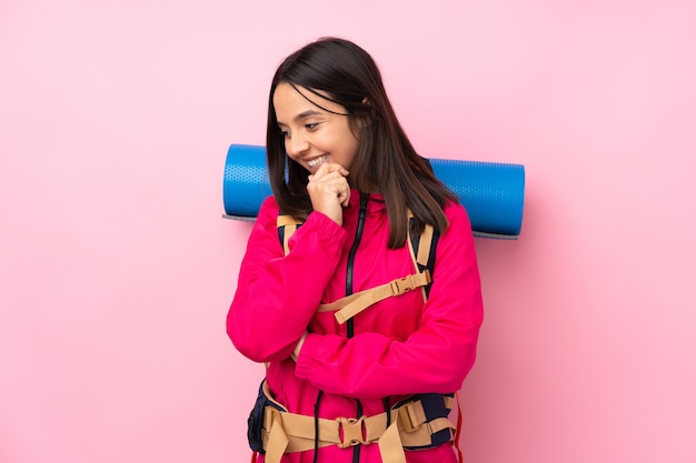 Young mountaineer girl with a big backpack over isolated pink wall looking to the side