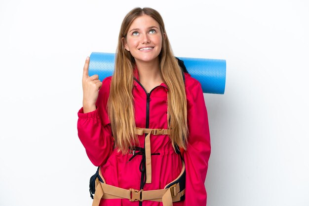 Young mountaineer girl with a big backpack over isolated white background pointing up and surprised