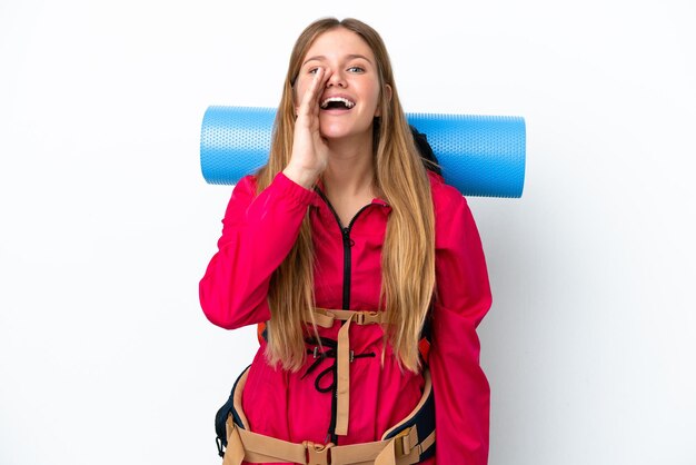 Young mountaineer girl with a big backpack over isolated white background shouting with mouth wide open