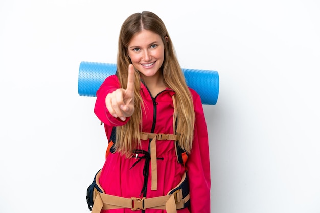 Young mountaineer girl with a big backpack over isolated white background showing and lifting a finger