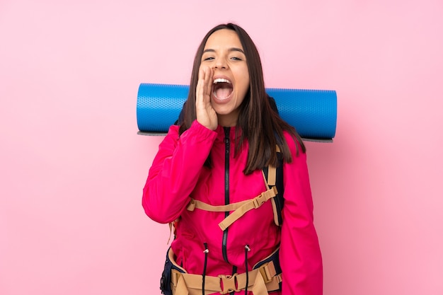 Young mountaineer girl with a big backpack over pink shouting with mouth wide open