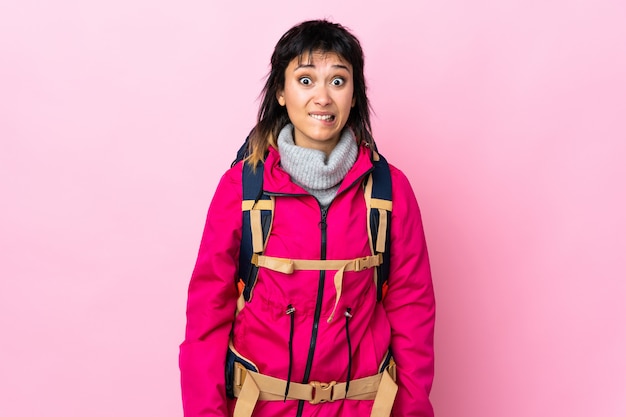 Ragazza giovane alpinista con un grande zaino sul muro rosa con dubbi e con espressione faccia confusa