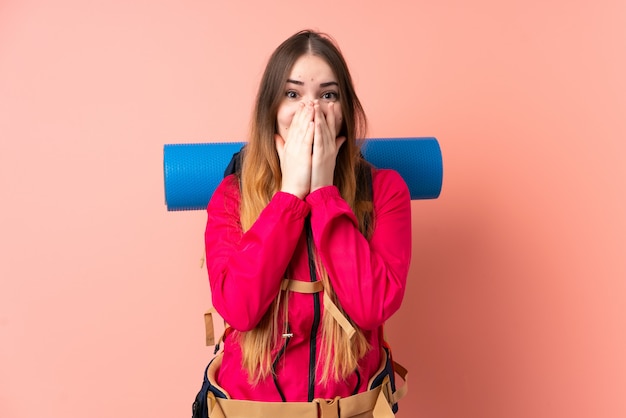 Young mountaineer girl with a big backpack on pink wall with surprise facial expression