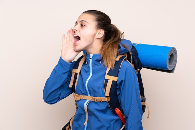 Young mountaineer girl with a big backpack shouting with mouth wide open