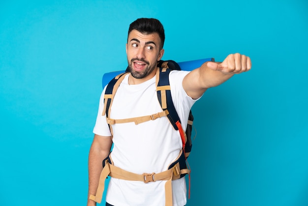 Young mountaineer man over isolated blue wall giving a thumbs up gesture