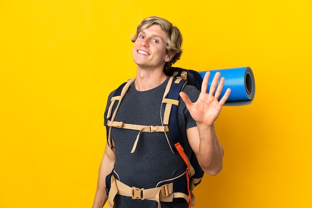 Молодой альпинист над изолированной желтой стеной салютует рукой со счастливым выражением лица