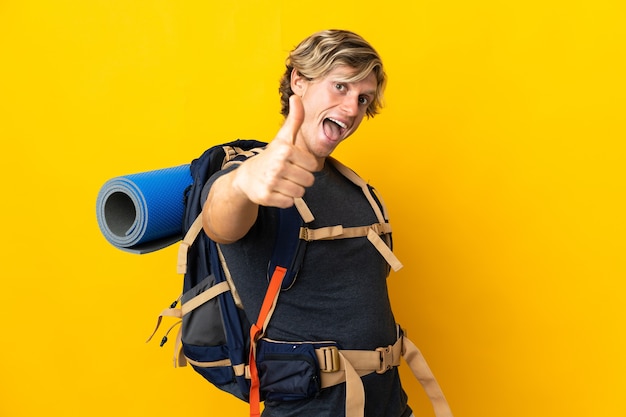 Young mountaineer man over isolated yellow wall with thumbs up because something good has happened