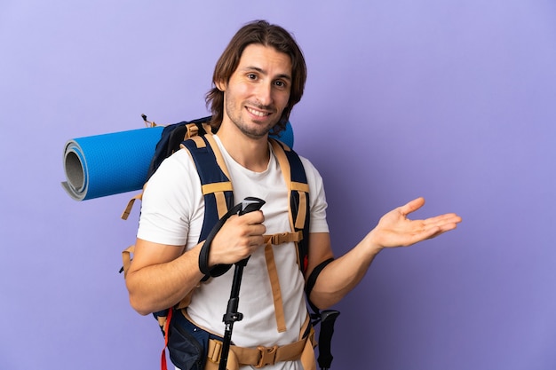 Photo young mountaineer man with a big backpack extending hands to the side for inviting to come