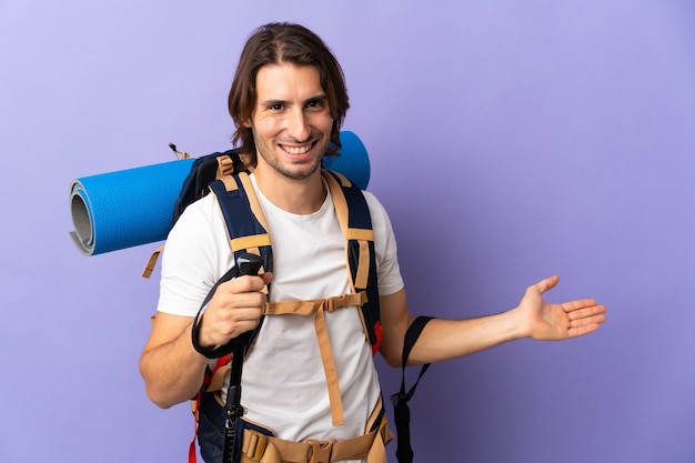 Young mountaineer man with a big backpack over isolated background extending hands to the side for inviting to come