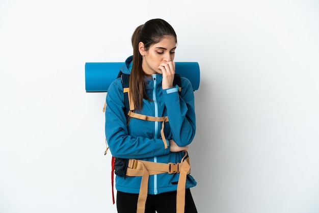 Young mountaineer man with a big backpack over isolated background having doubts