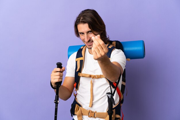 Young mountaineer man with a big backpack over isolated background making money gesture