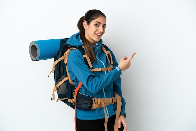 Young mountaineer man with a big backpack over isolated background pointing back