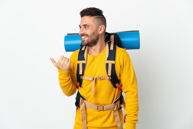 Young mountaineer man with a big backpack over isolated background pointing to the side to present a product