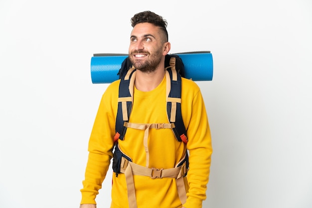 Young mountaineer man with a big backpack over isolated background thinking an idea while looking up