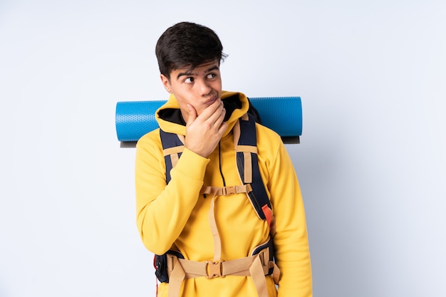 Young mountaineer man with a big backpack over isolated blue thinking an idea