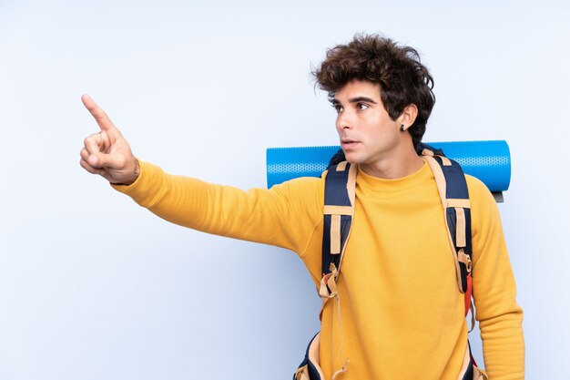 Young mountaineer man with a big backpack over isolated blue wall touching on transparent screen