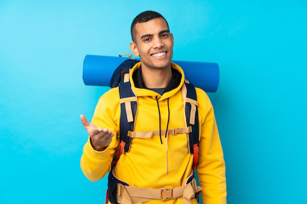 Young mountaineer man with a big backpack over isolated blue wallhandshaking after good deal