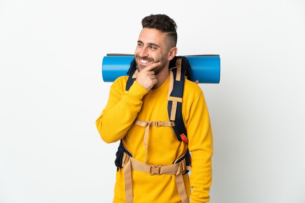 Young mountaineer man with a big backpack over isolated looking to the side and smiling