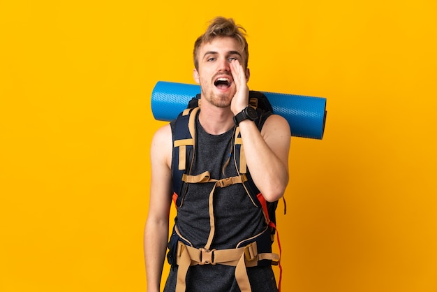Young mountaineer man with a big backpack isolated shouting with mouth wide open