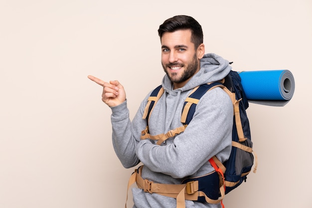 Young mountaineer man with a big backpack over isolated wall