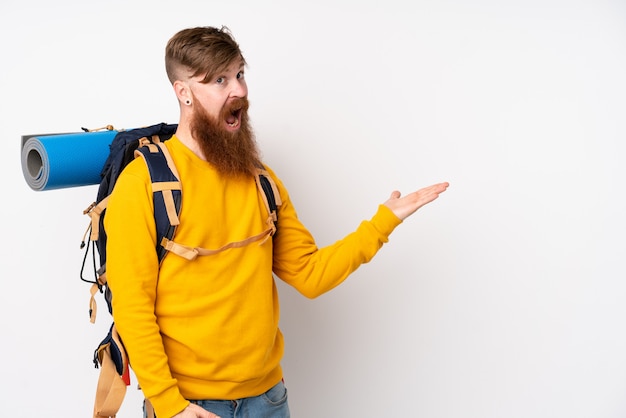 Молодой человек альпиниста с большим рюкзаком над изолированной белой стеной, протягивающей руки в сторону для приглашения прийти
