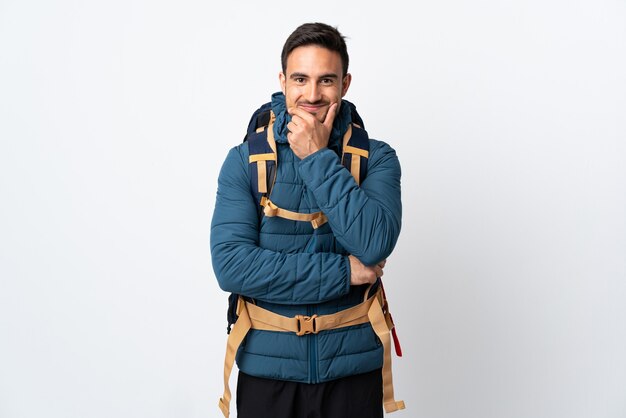 Young mountaineer man with a big backpack isolated on white wall laughing