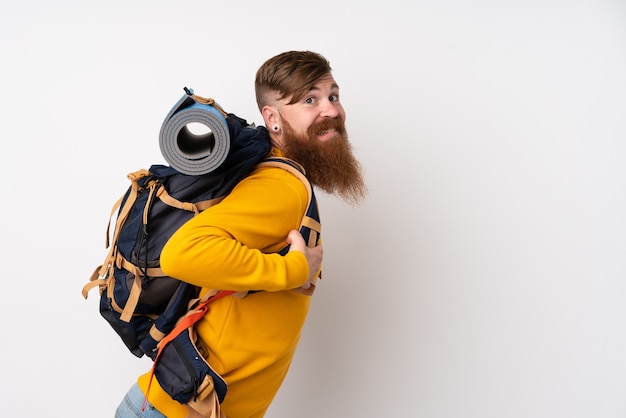 Young mountaineer man with a big backpack over isolated white wall