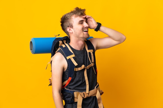 Young mountaineer man with a big backpack isolated on yellow background smiling a lot