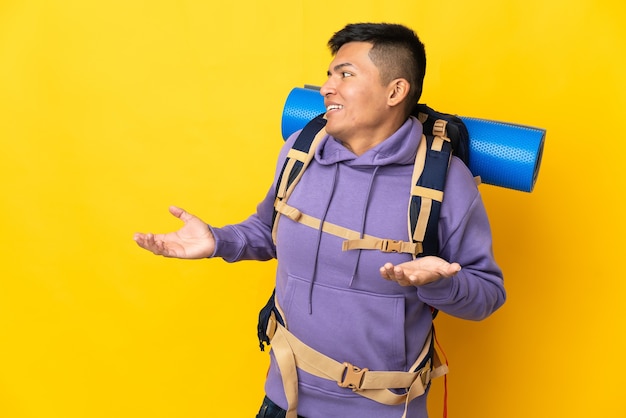 側を見ながら驚きの表情で黄色の背景に分離された大きなバックパックを持つ若い登山家の男