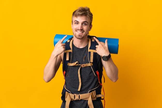 Young mountaineer man with a big backpack isolated on yellow giving a thumbs up gesture