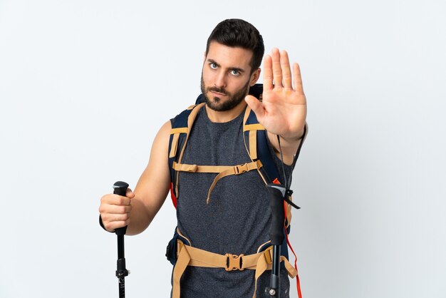 Young mountaineer man with a big backpack and trekking poles isolated on white background making stop gesture with her hand