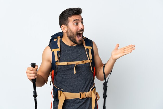 Young mountaineer man with a big backpack and trekking poles isolated on white background with surprise facial expression