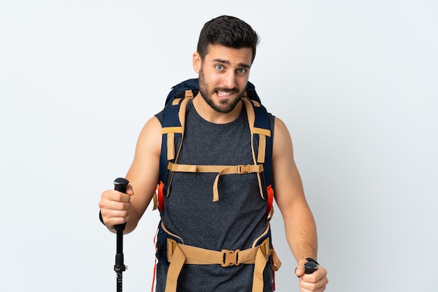 Young mountaineer man with a big backpack and trekking poles isolated on white having doubts and with confuse face expression