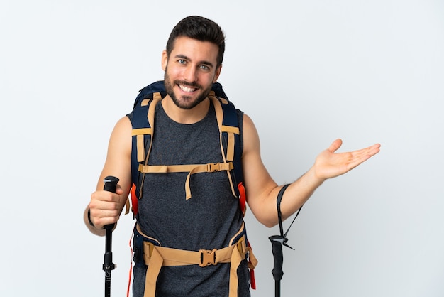 Young mountaineer man with a big backpack and trekking poles isolated on white holding copyspace imaginary on the palm