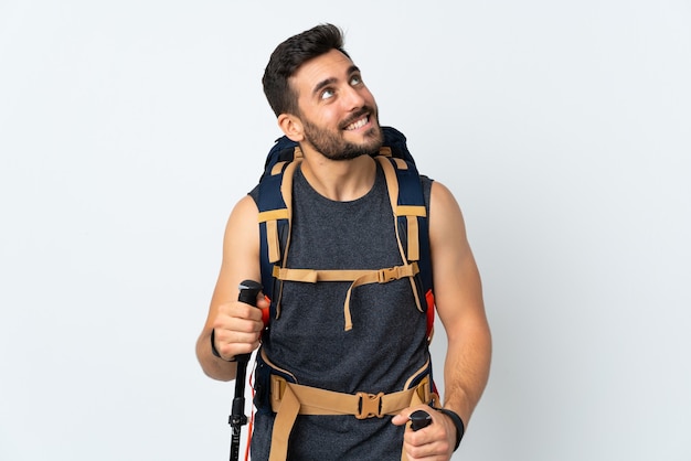 Молодой альпинист с большим рюкзаком и треккинговыми палками, изолированными на белом, смеется и смотрит вверх