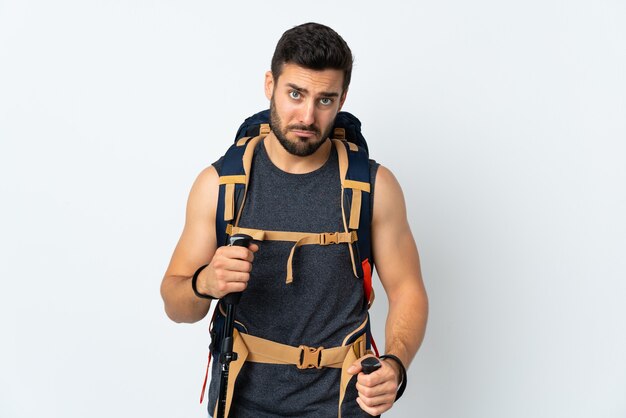 Young mountaineer man with a big backpack and trekking poles isolated on white pleading