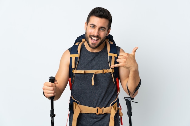 Young mountaineer man with a big backpack and trekking poles isolated on white wall making phone gesture