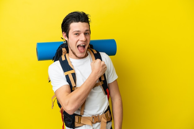 Young mountaineer Russian man with a big backpack isolated on yellow surface celebrating a victory