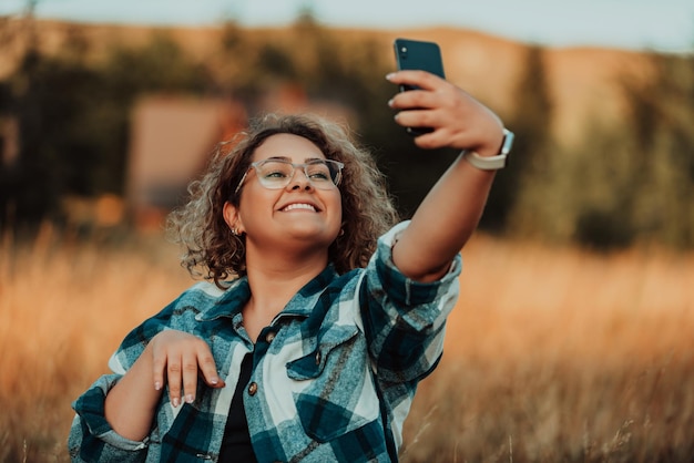 A young mountaineer sits on a rock after climbing a mountain and takes a photo with her smartphone